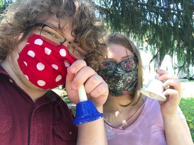 A man and a woman wearing face masks are holding bells.
