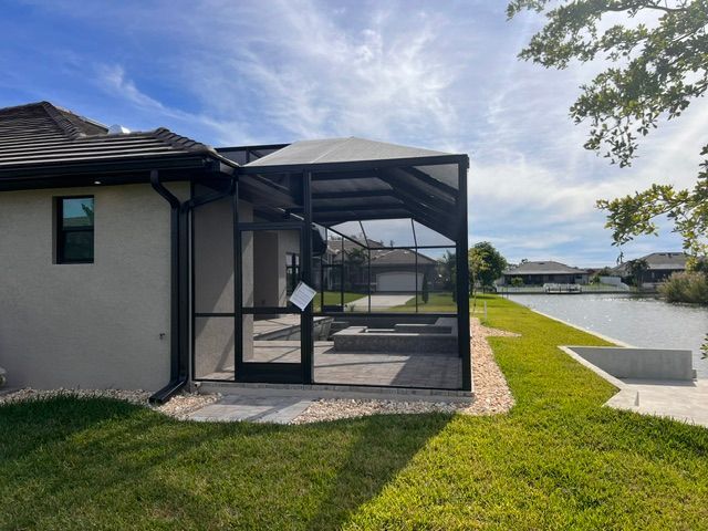 Screened patio beside a house overlooking a canal, with green lawn and cloudy sky