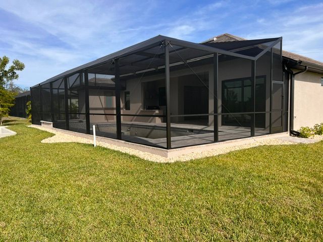 Screened patio attached to a beige house beside a green lawn under a clear sky