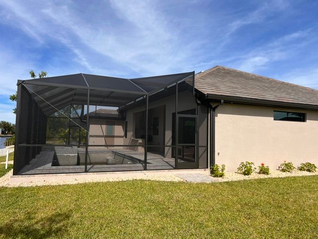 Screened patio enclosure beside a tan house, with green lawn and blue sky.