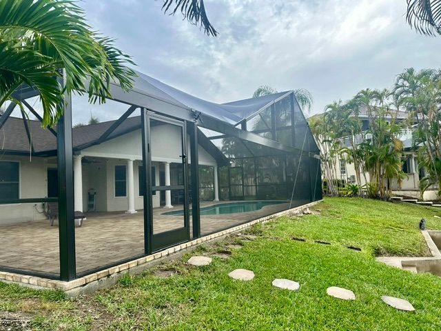 Modern house with a screened patio, green lawn, stepping stones, and palm trees in a tropical setting