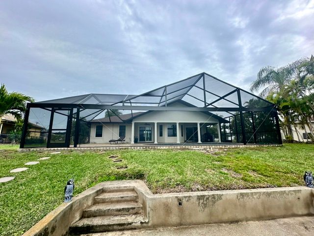 House with large screened enclosure and green lawn under cloudy sky