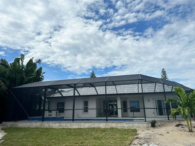 Small white building with a dark roof and screened porch, set on a grassy lot under a cloudy blue sky