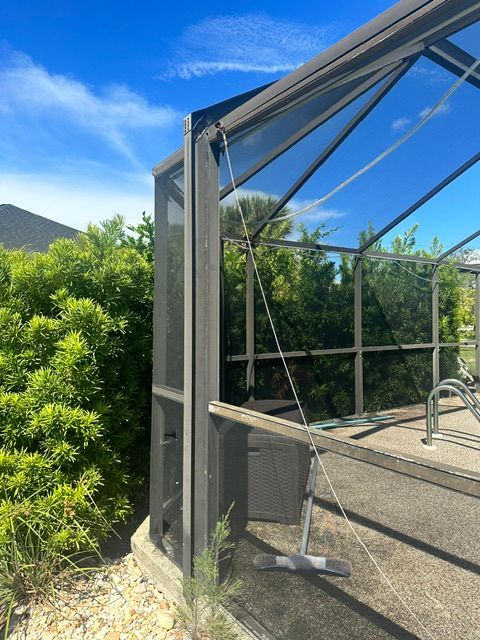 Open greenhouse door with metal frame beside lush green bushes under a blue sky