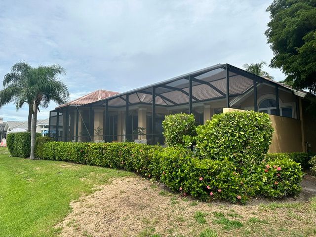 Single-story house with screened porch, green lawn, hedges, and a palm tree under a cloudy sky