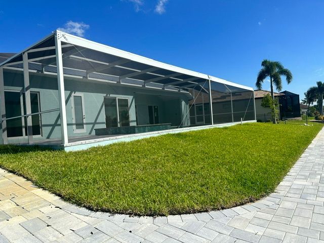 Modern white house with screened patio, green lawn, and paved walkway under a blue sky
