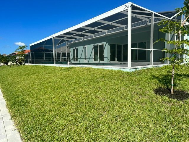 Modern glass building with white beams beside a sunny green lawn and blue sky