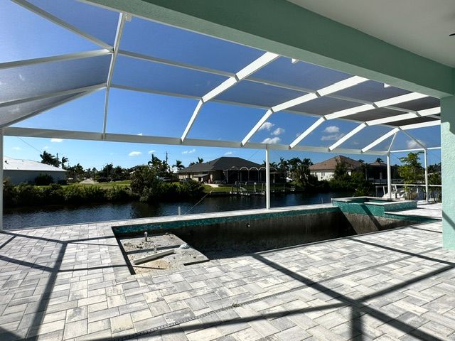 Covered poolside patio with screened roof, blue water, and sunny tropical landscape beyond