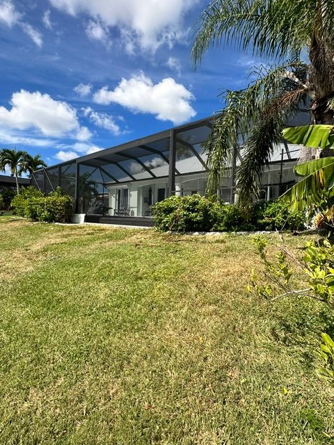 Modern house with screened patio, green lawn, palm trees, and blue sky with clouds