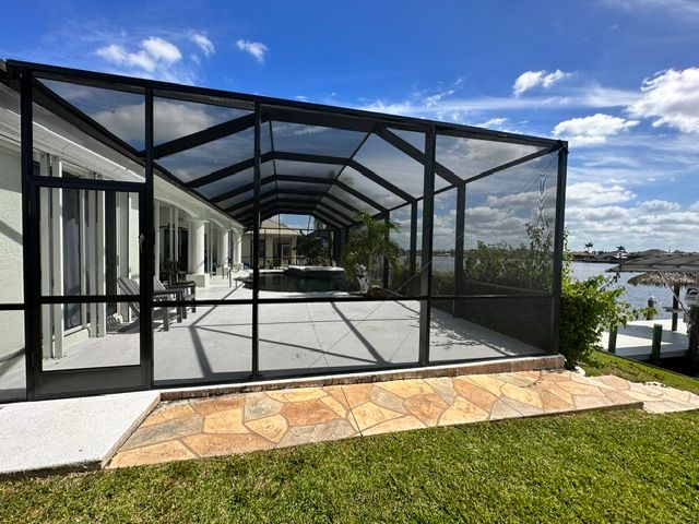 Screened patio with black metal frame and stone walkway beside a waterfront house under a blue sky