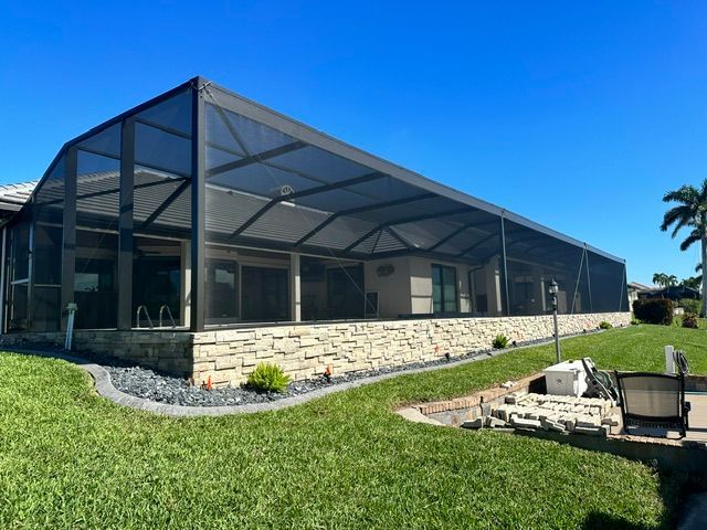 Screened patio on a stone house beside a green lawn under a bright blue sky