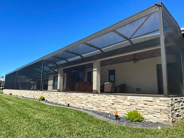 Covered patio with black screen enclosure, stone wall, and green lawn under a blue sky
