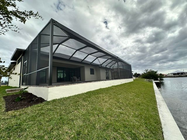 Modern waterfront house with screened porch, white foundation, and grassy lawn beside the water under cloudy skies
