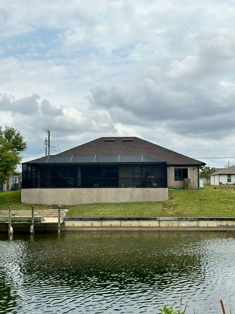 House with screened porch beside a waterfront and dock under cloudy sky