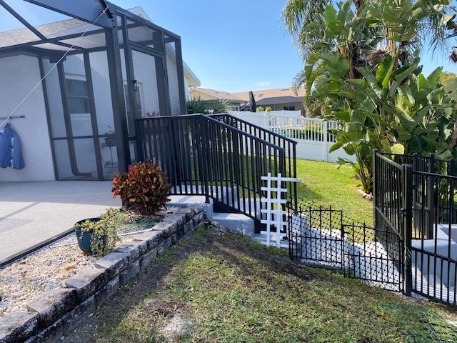 Backyard patio with screened enclosure, black metal fence, tropical plants, and a grassy lawn