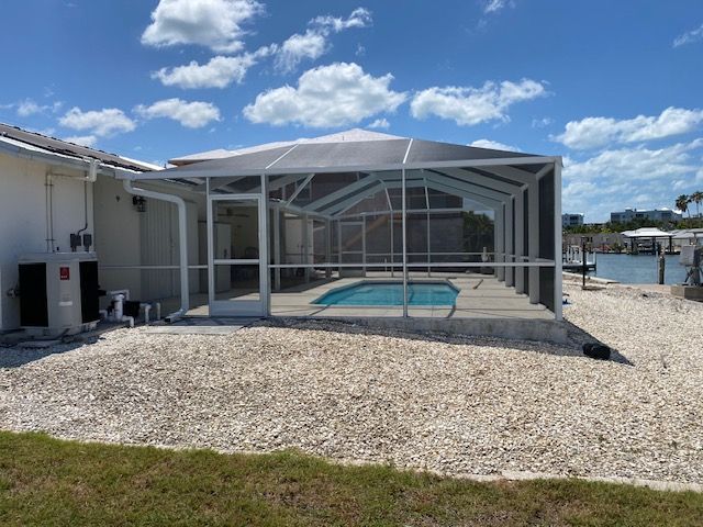 Screened-in patio with a small pool, white house exterior, and gravel yard under a blue sky