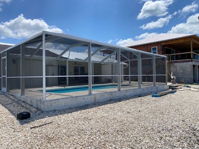 Screened-in backyard pool enclosure beside a house under a blue sky