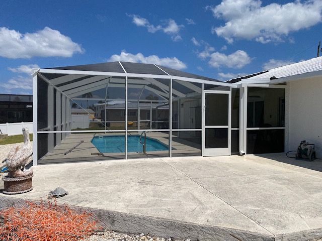 Enclosed swimming pool beneath a white screened patio on a sunny day.