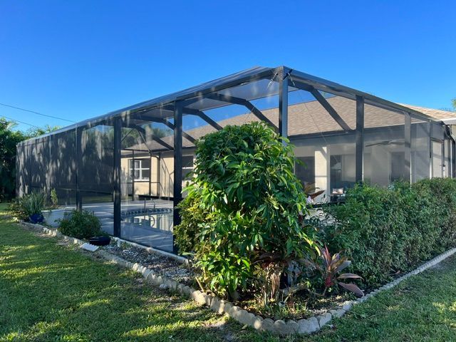 Screened patio with black frame, surrounded by green shrubs and grass under a blue sky