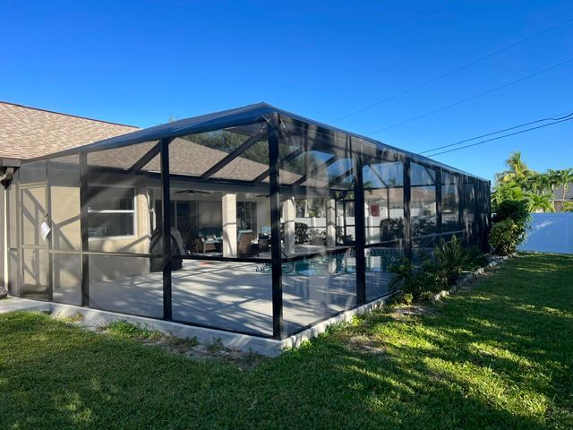 Black screened patio enclosure attached to a house, beside a green lawn under a blue sky