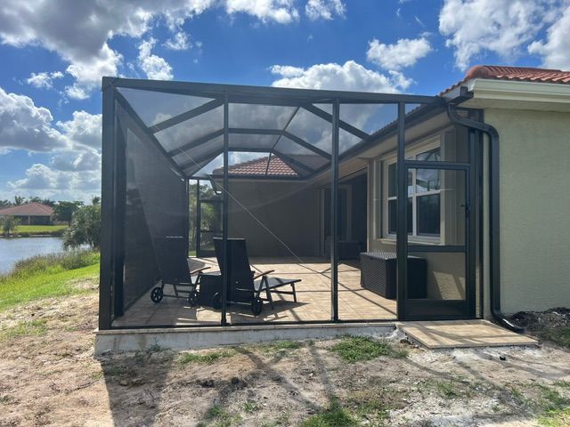 Screened patio enclosure with chairs beside a house and lake under a partly cloudy sky