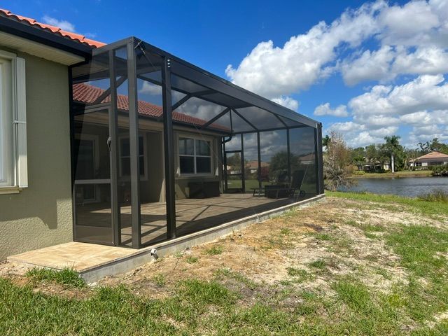 Screened patio enclosure beside a house overlooking a grassy yard and lake under a blue sky