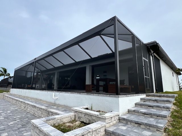 Modern house with black-framed glass walls, a raised patio, and stone steps on a sloped driveway