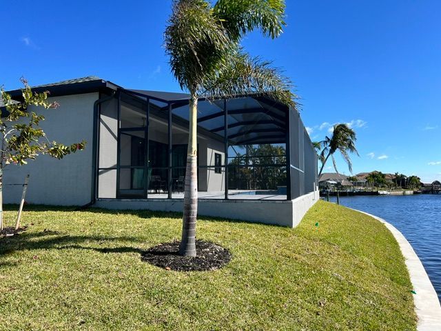 Modern house with screened patio beside a canal, grassy lawn, and palm trees under a clear blue sky