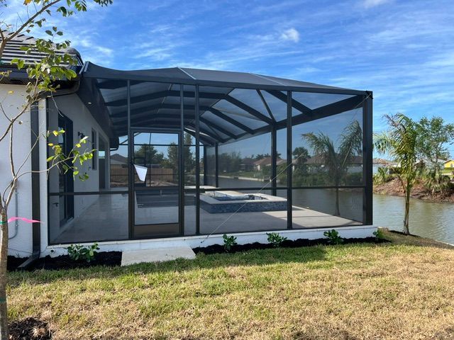 Screened patio enclosure beside a house, overlooking a grassy yard and pond under a blue sky