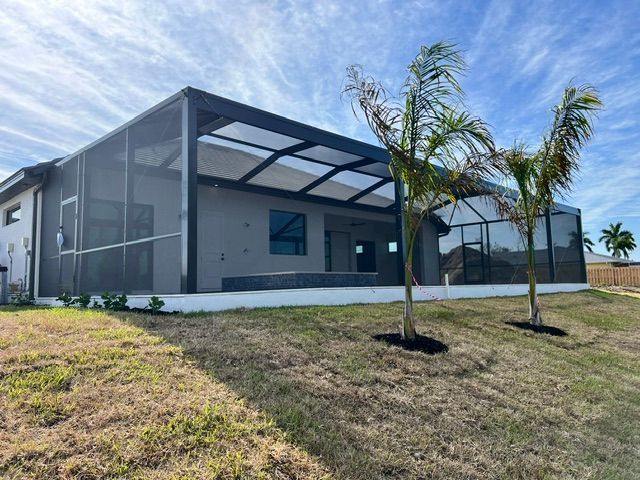 Modern gray screened-in patio beside a white house with palm trees and a grassy yard