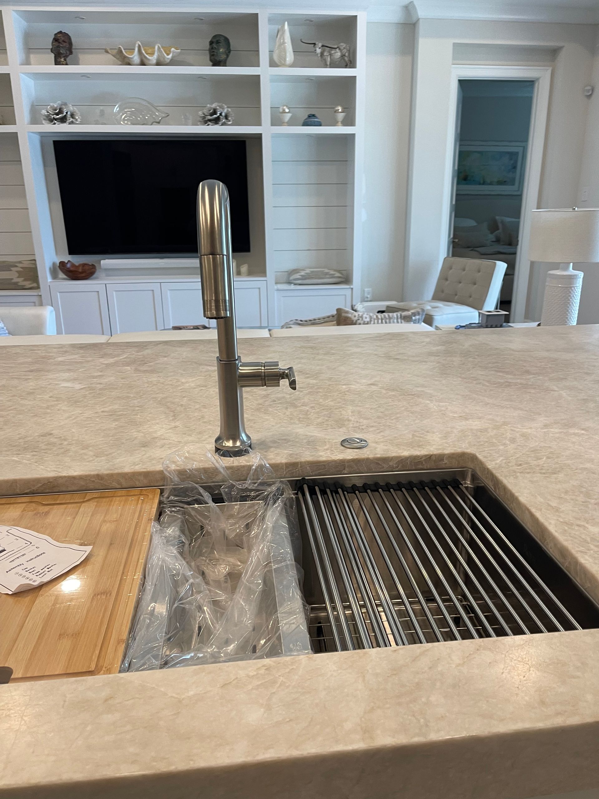 A kitchen sink with a cutting board and a television in the background.