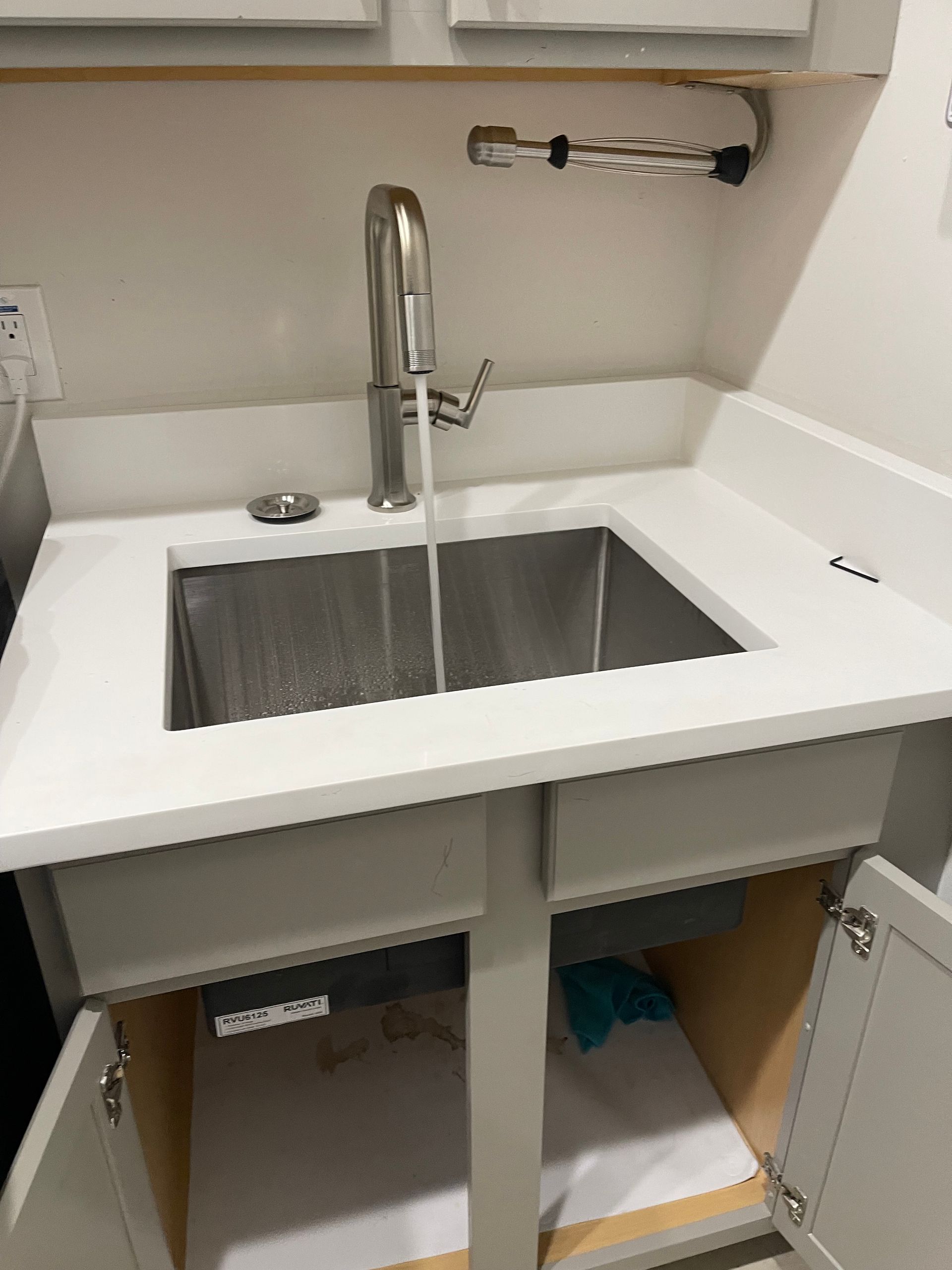 A kitchen sink with the door open and water running out of it.