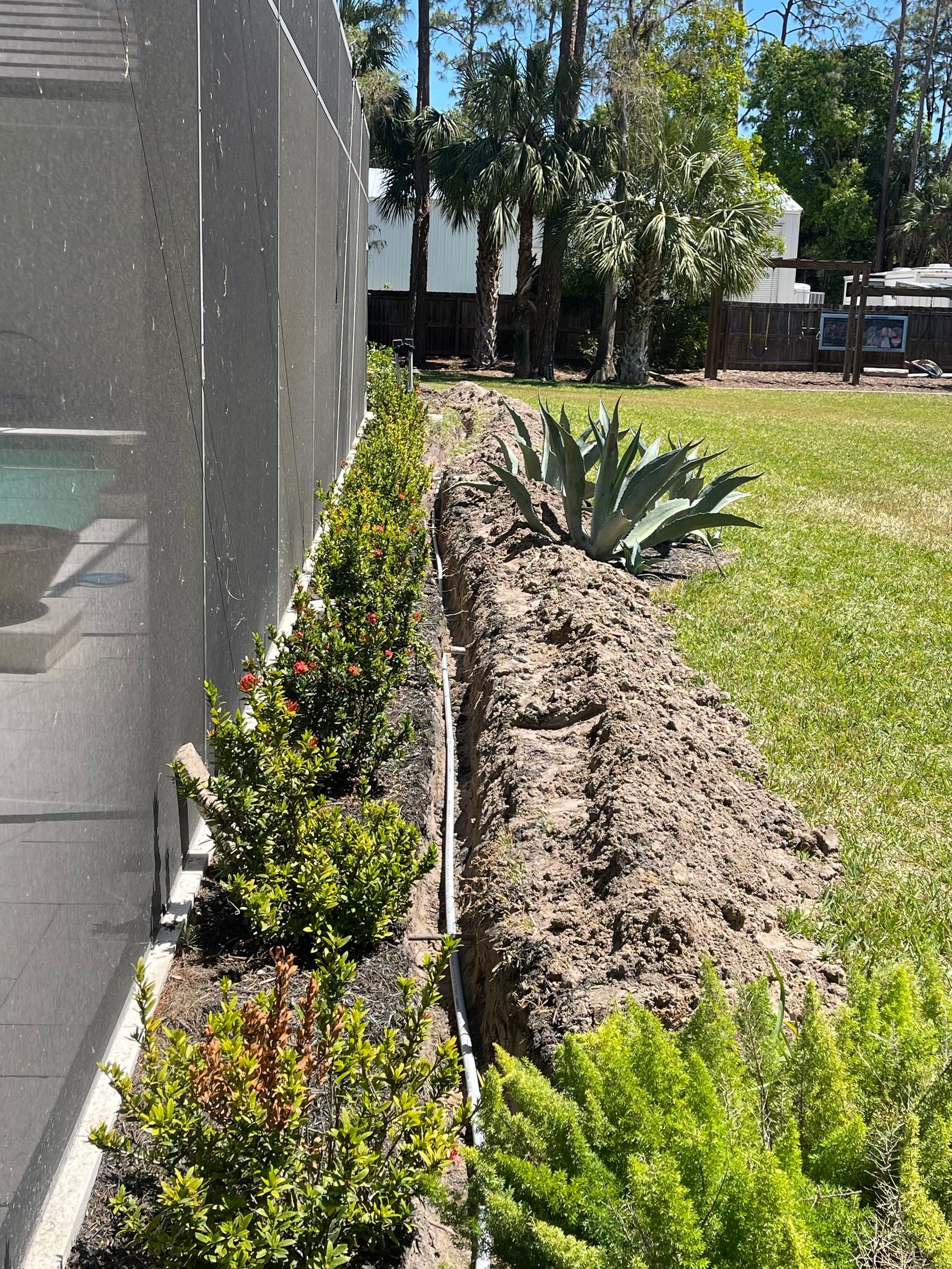 A garden with a fence and a pool in the background.