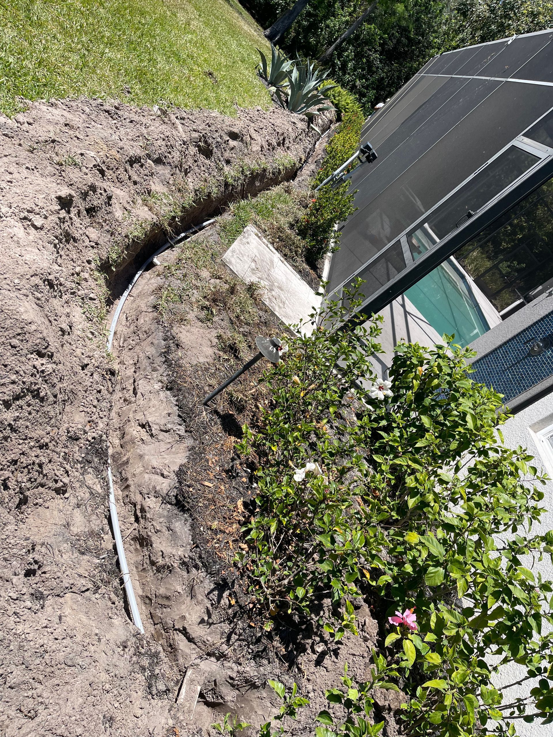 A hose is laying in the dirt next to a swimming pool.