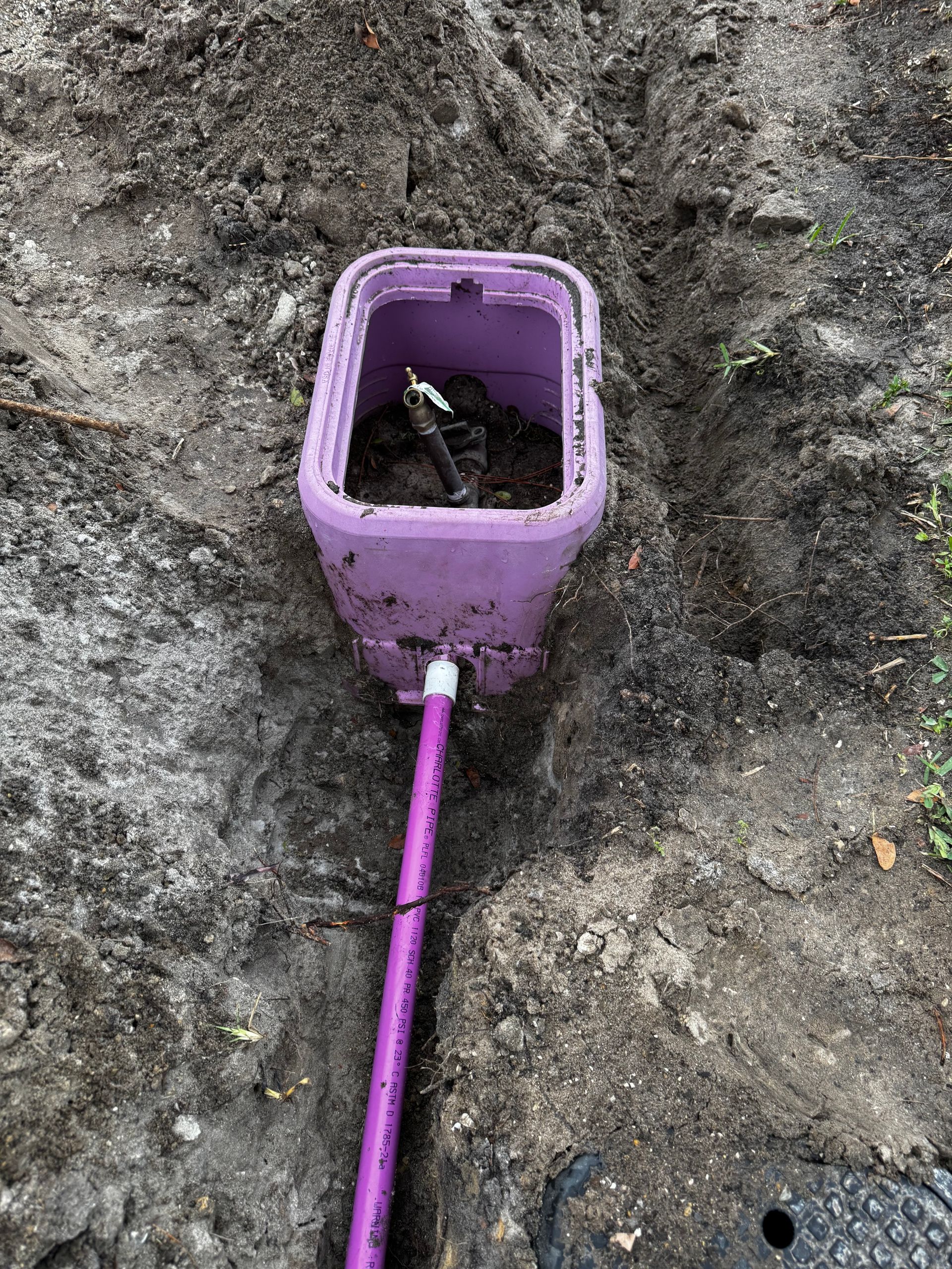 A purple box is sitting in the dirt next to a purple pipe.