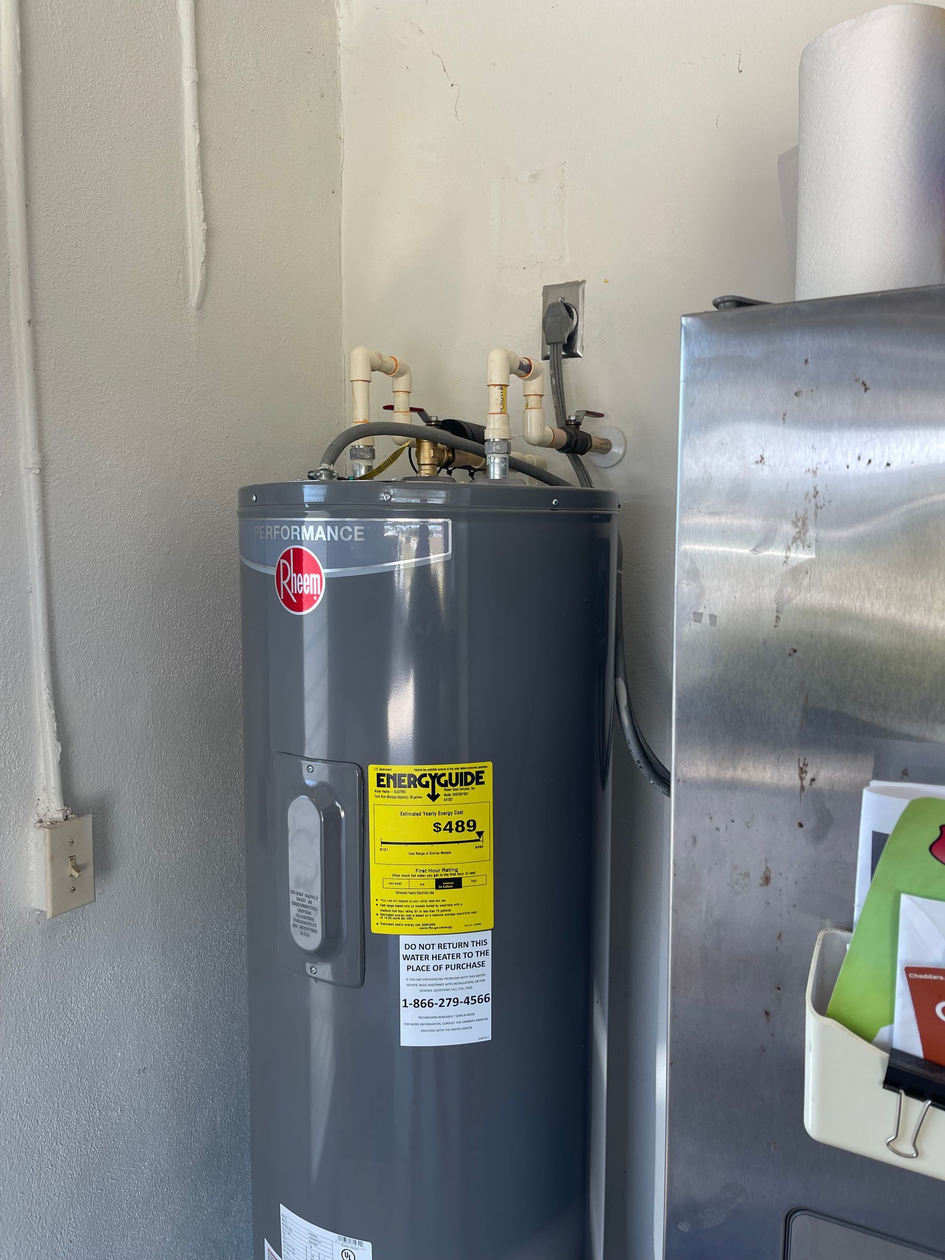 A gray water heater is sitting next to a stainless steel refrigerator.