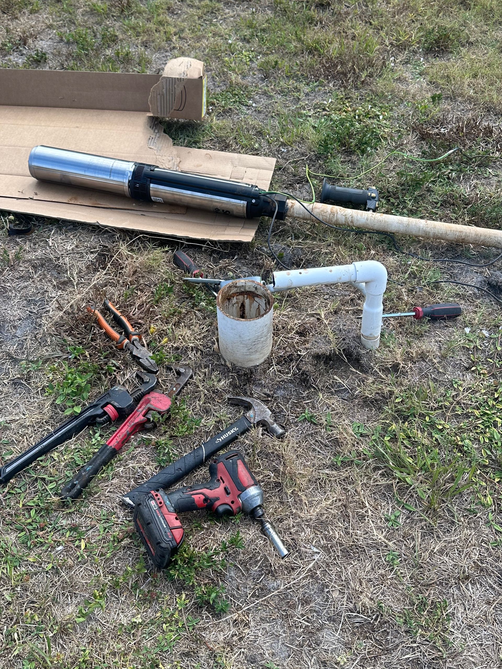 A bunch of tools are laying on the ground in the grass.