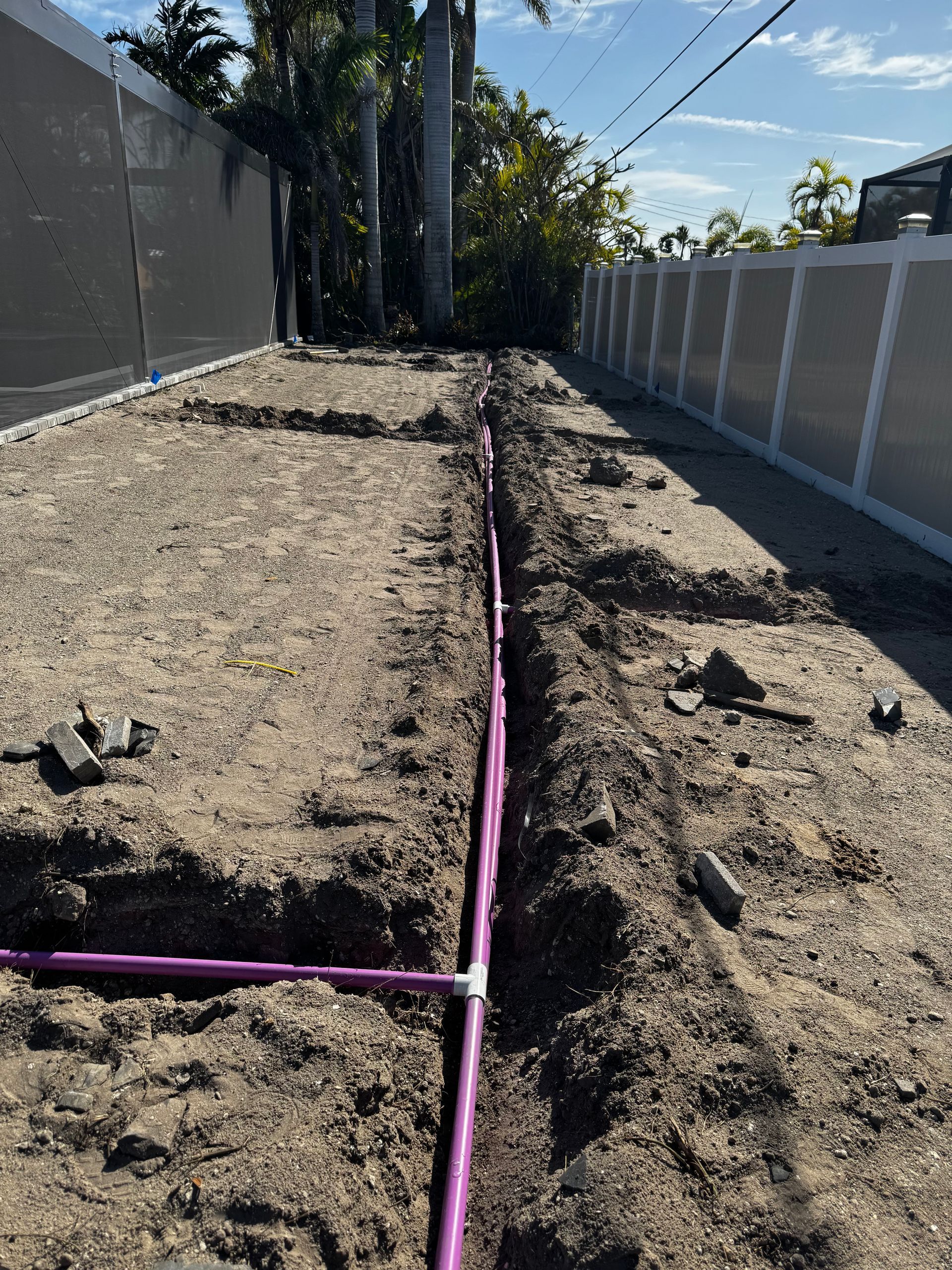 A purple pipe is laying in the dirt next to a fence.
