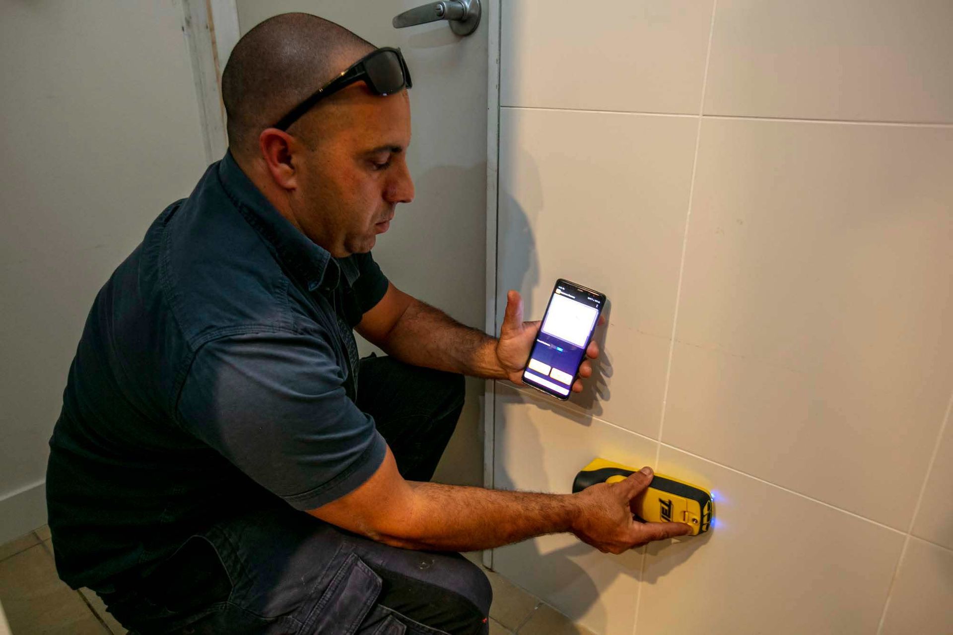 A Man is Using a Cell Phone to Measure a Wall — Superior Termite & Pest Control in Bundaberg, QLD
