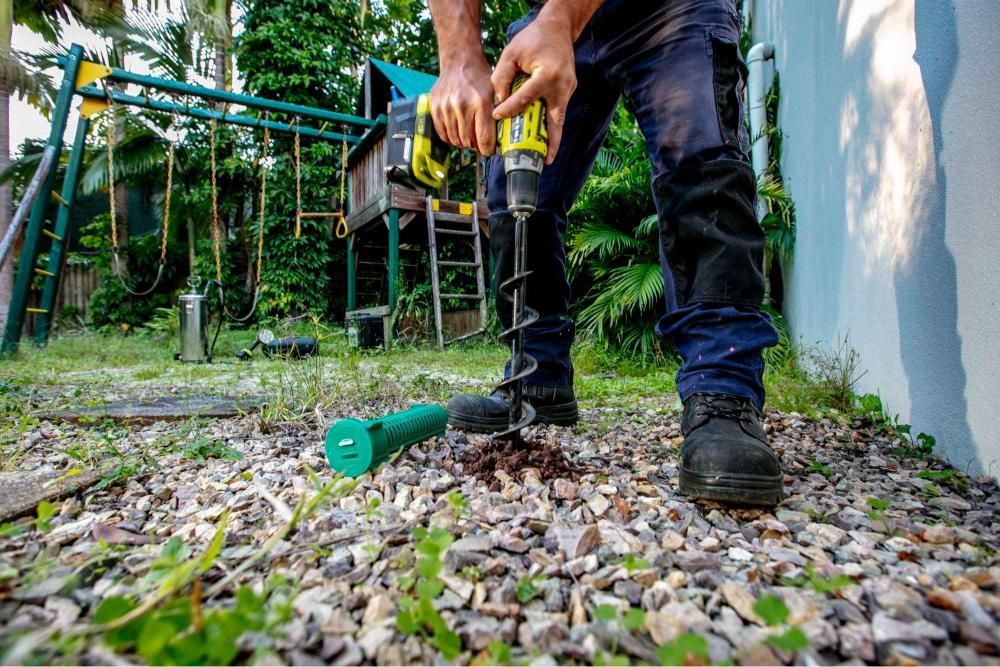 A Man is Using a Drill to Drill a Hole in the Ground — Superior Termite & Pest Control in Noosa, QLD
