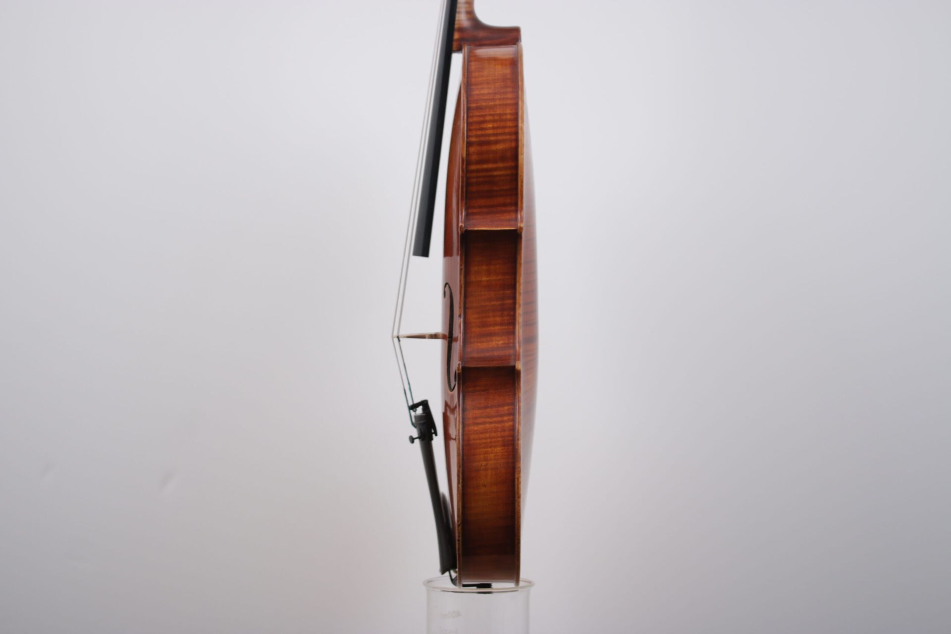 A violin is sitting on top of a clear glass container against a white wall.