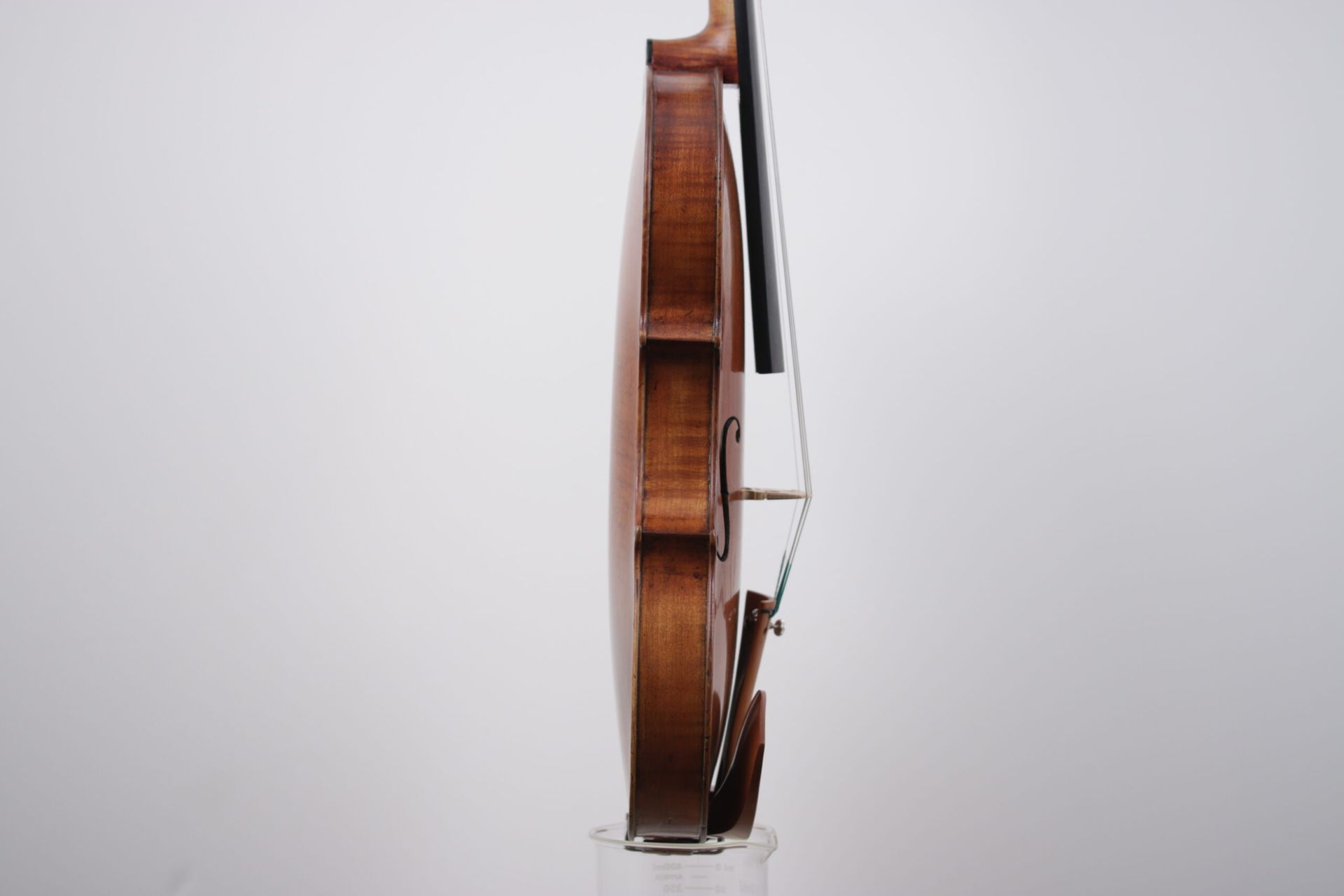A violin is sitting on a clear stand on a white background.