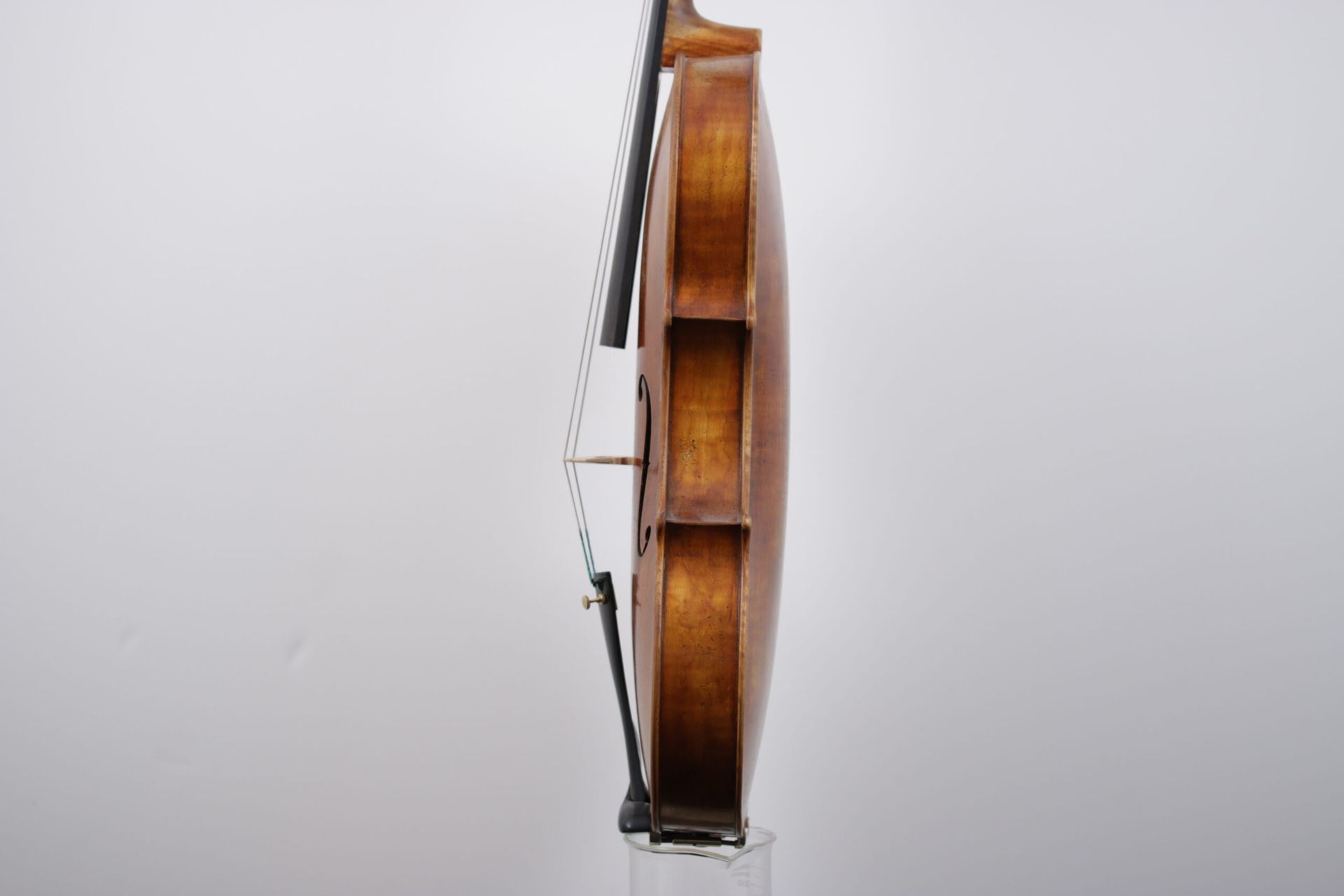 A violin is sitting on a glass stand on a white background.