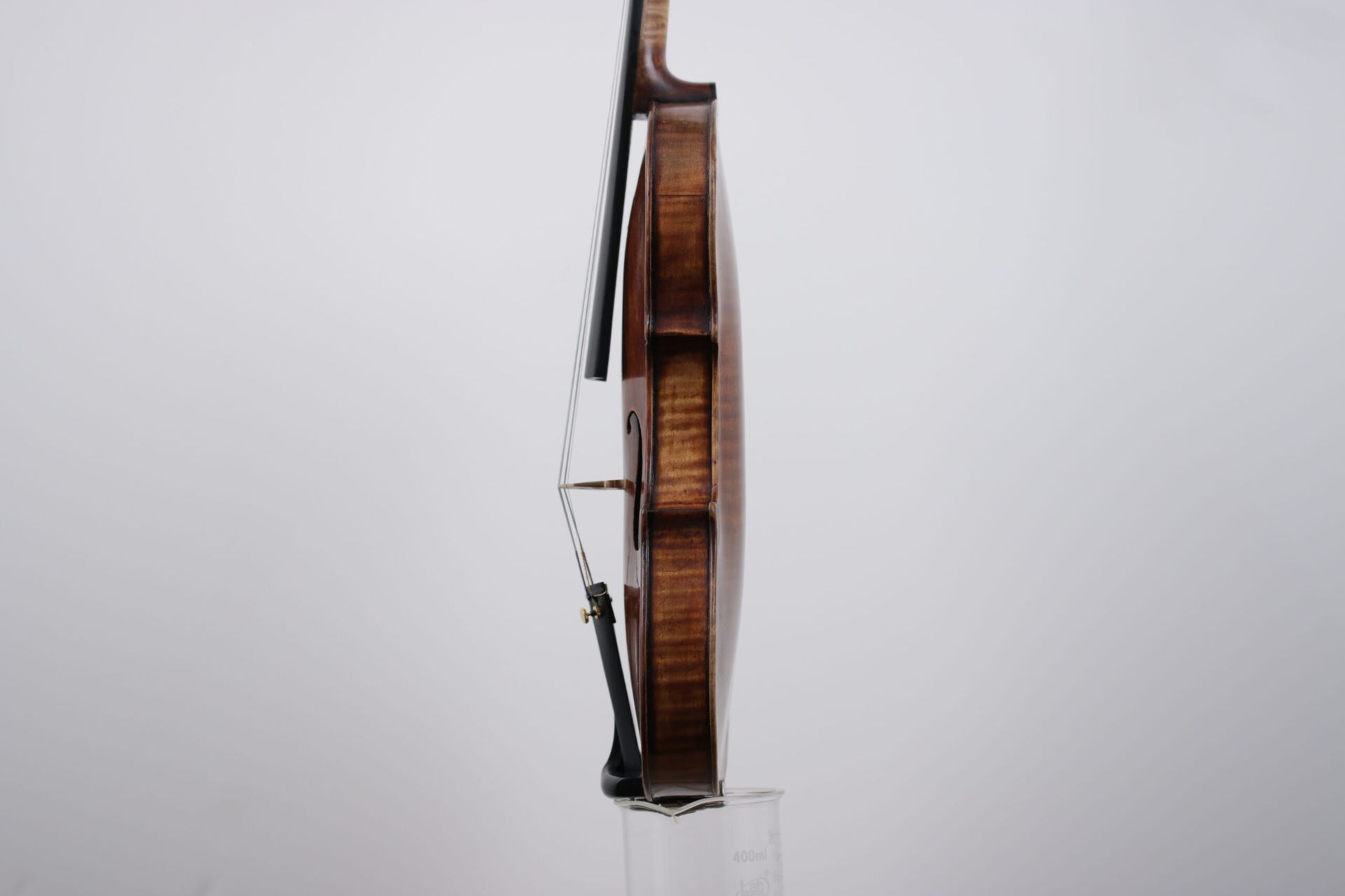 A violin is sitting on a glass stand on a white background.
