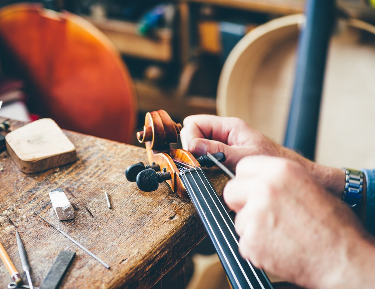 A person is working on a violin on a wooden table.