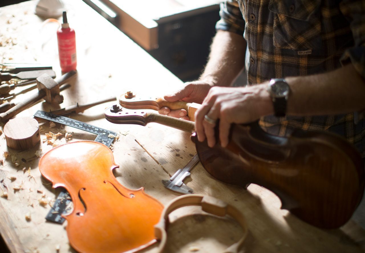 A man is working on a violin on a wooden table.