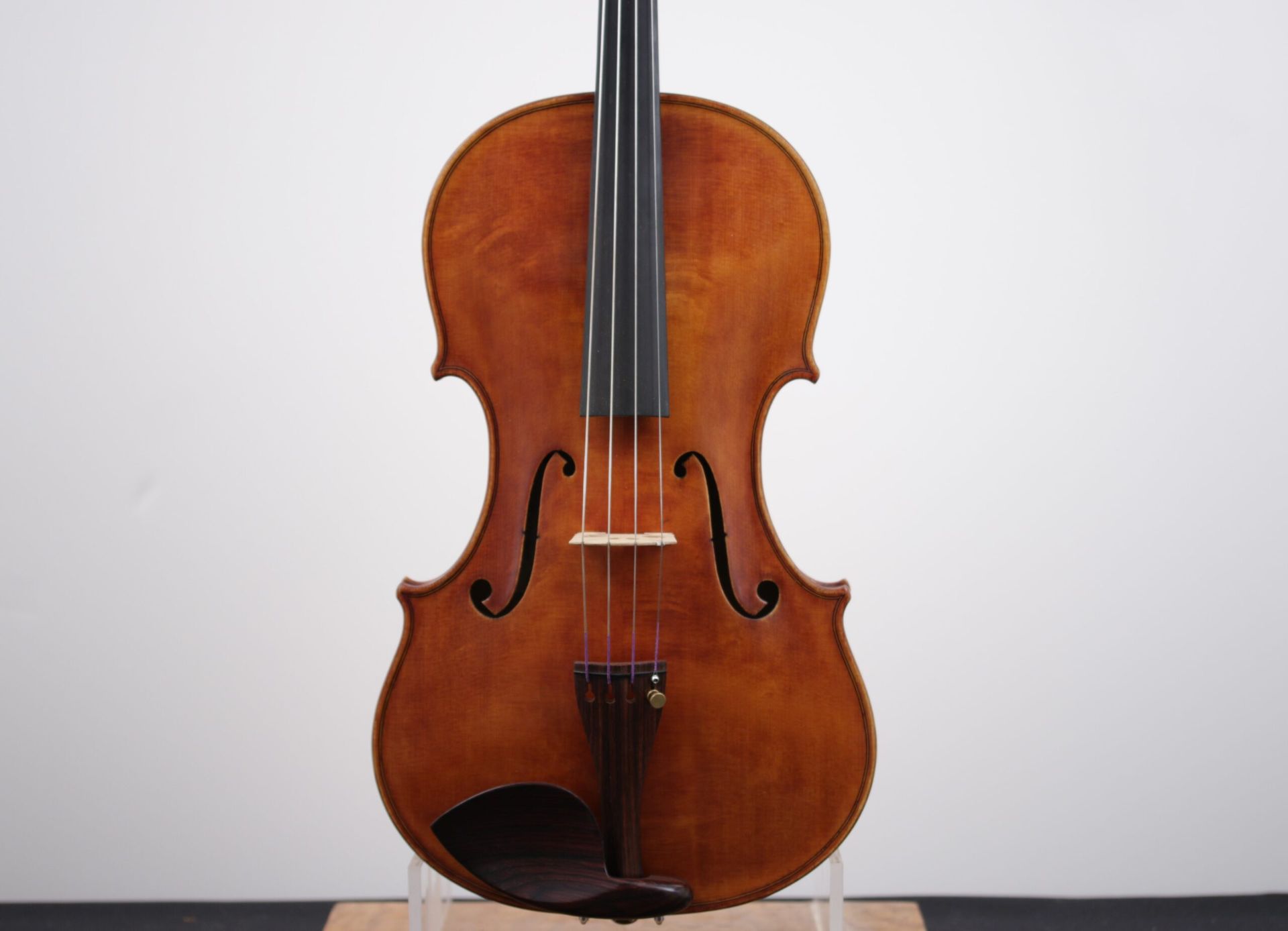 A violin is sitting on a wooden stand against a white background