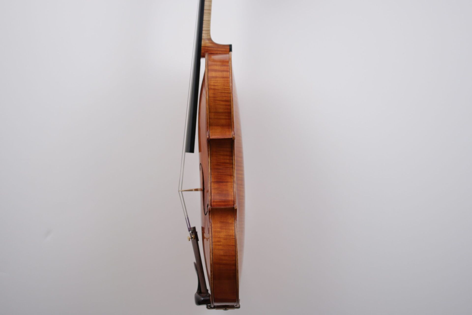 A violin with a bow is hanging on a white wall.