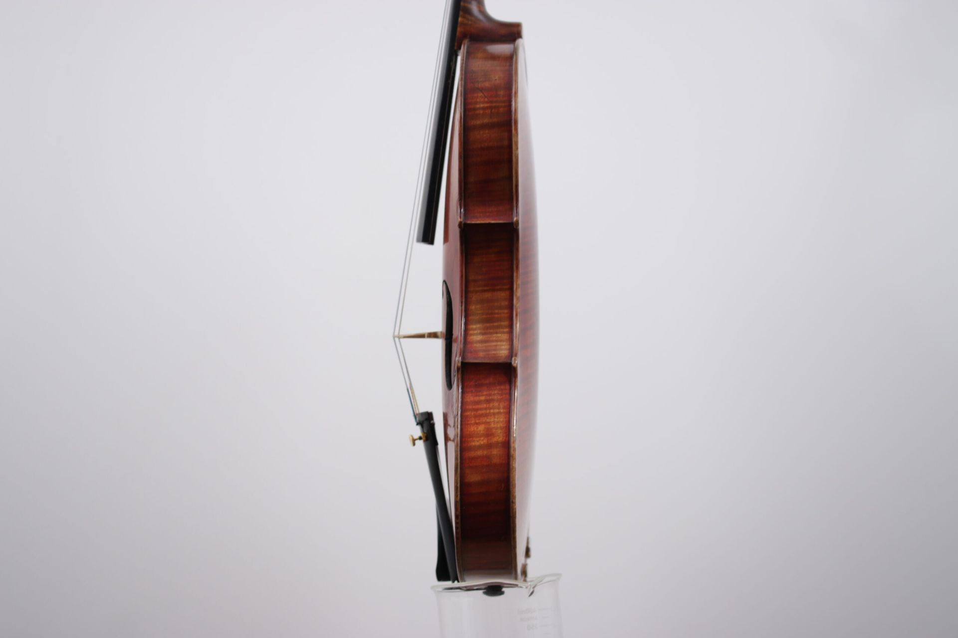 A violin is sitting on a clear display stand against a white wall.