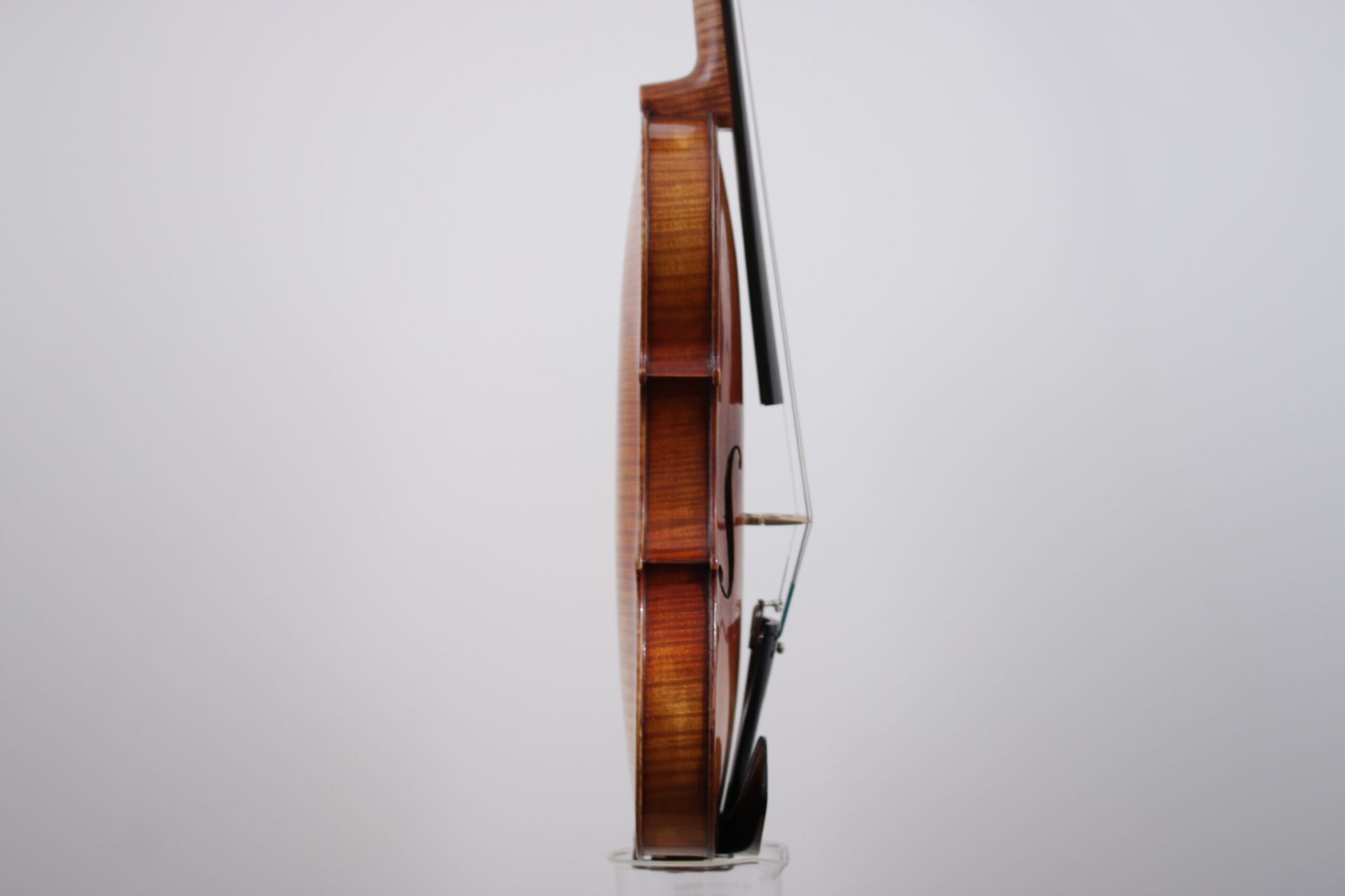 A violin is sitting on a glass stand on a white background.